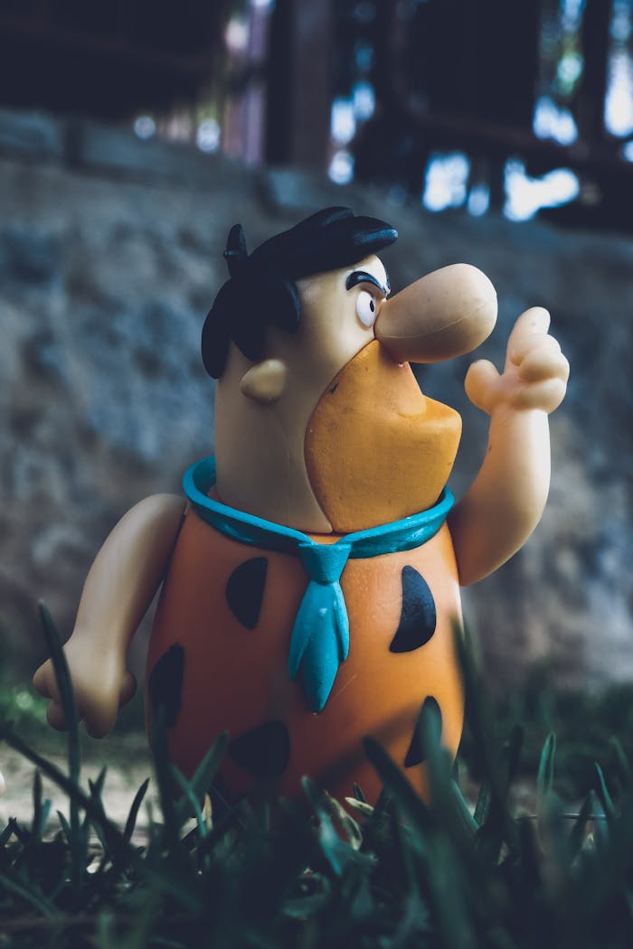 A close-up of a Freddie Flintstone action figure captured outdoors with a vintage feel.